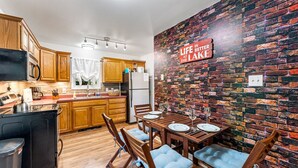 A modern kitchen with wooden cabinets, a dining table set for four, and a brick wall with a motivational quote.