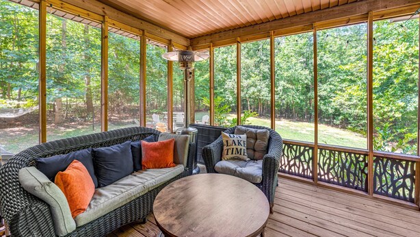 A covered outdoor seating area with wicker furniture and a round table, overlooking a wooded landscape.