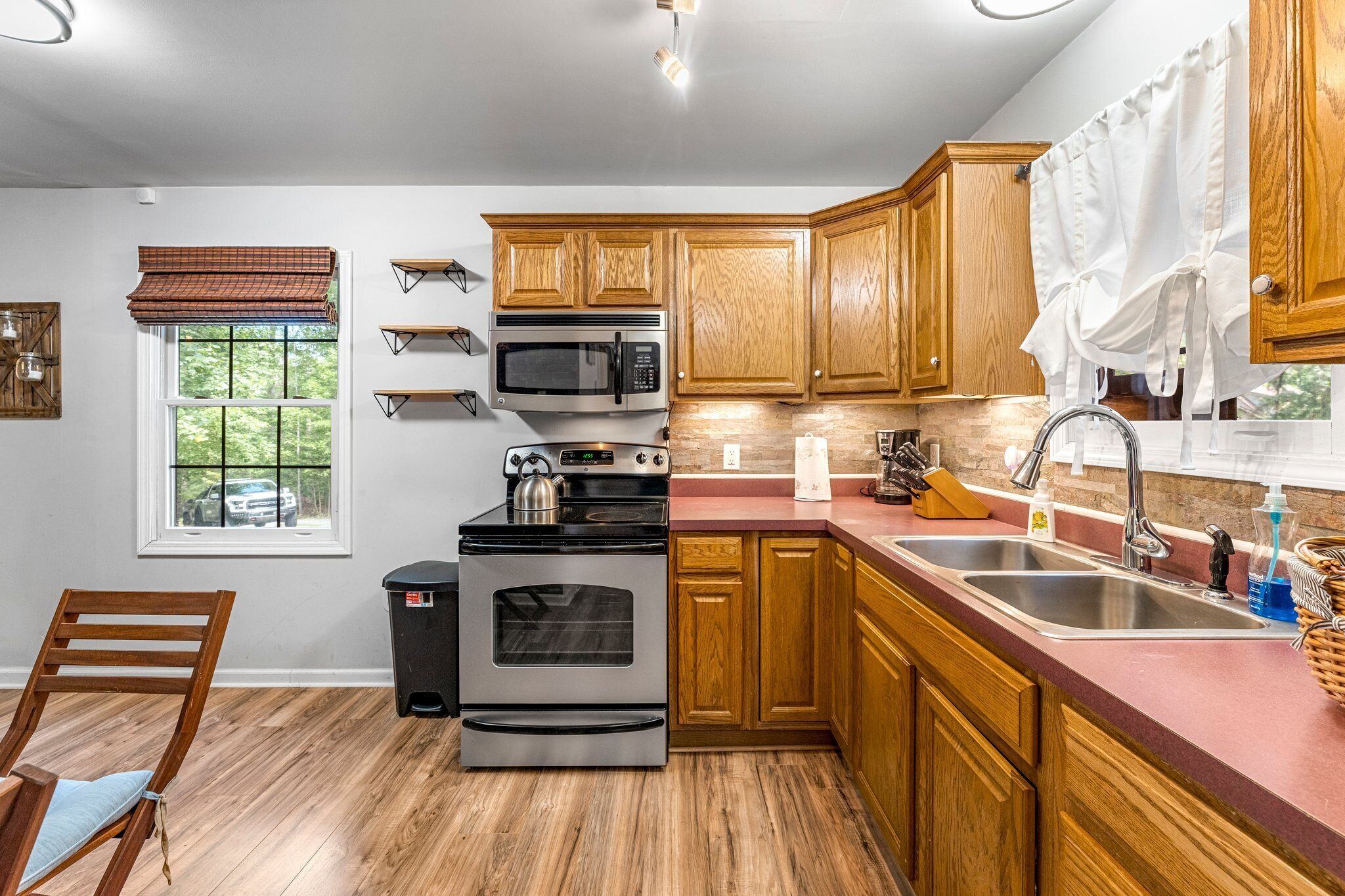 A kitchen with wooden cabinets, stainless steel appliances, a window with a view, and a chair.