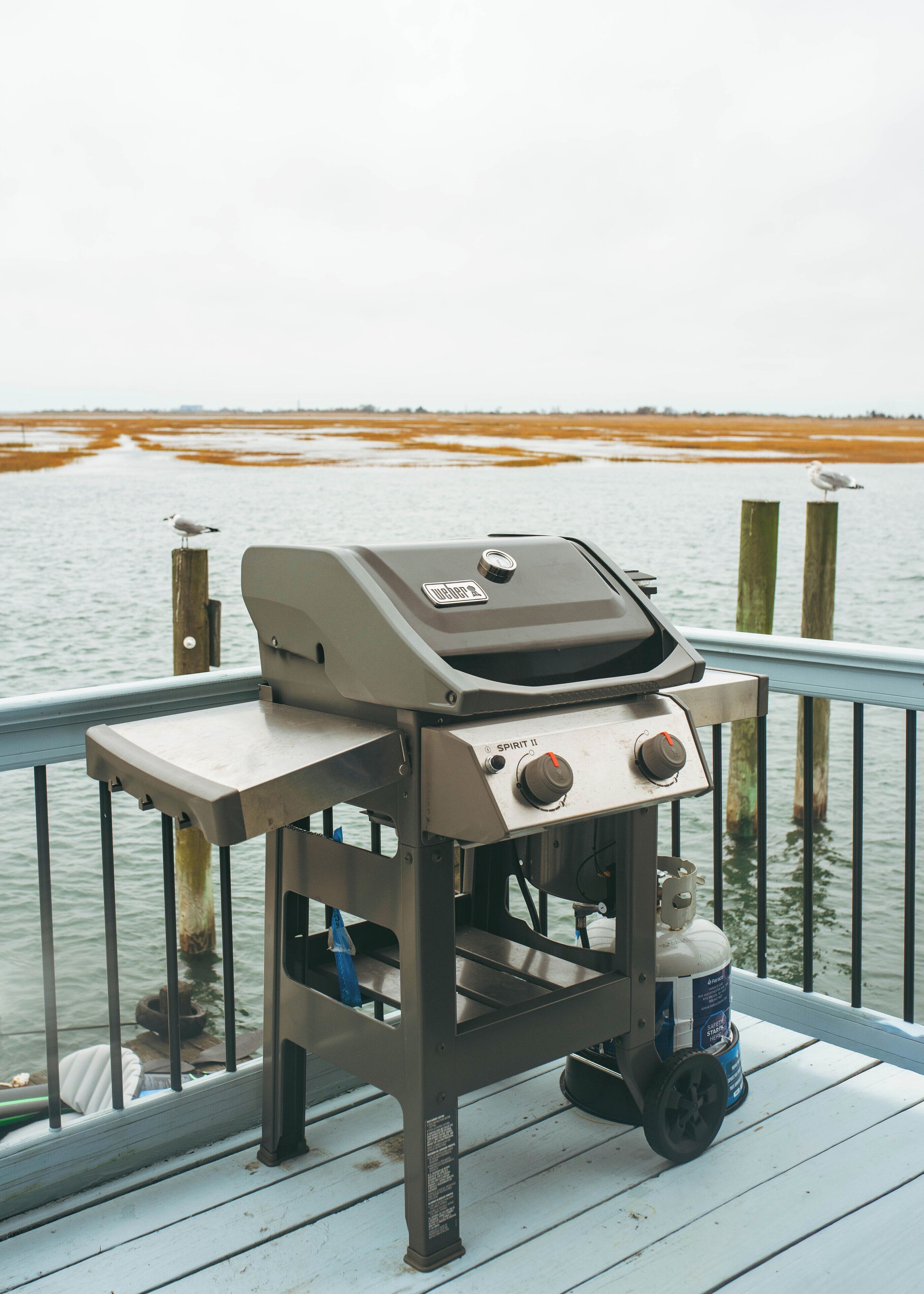 A barbecue grill on a wooden deck by a body of water.