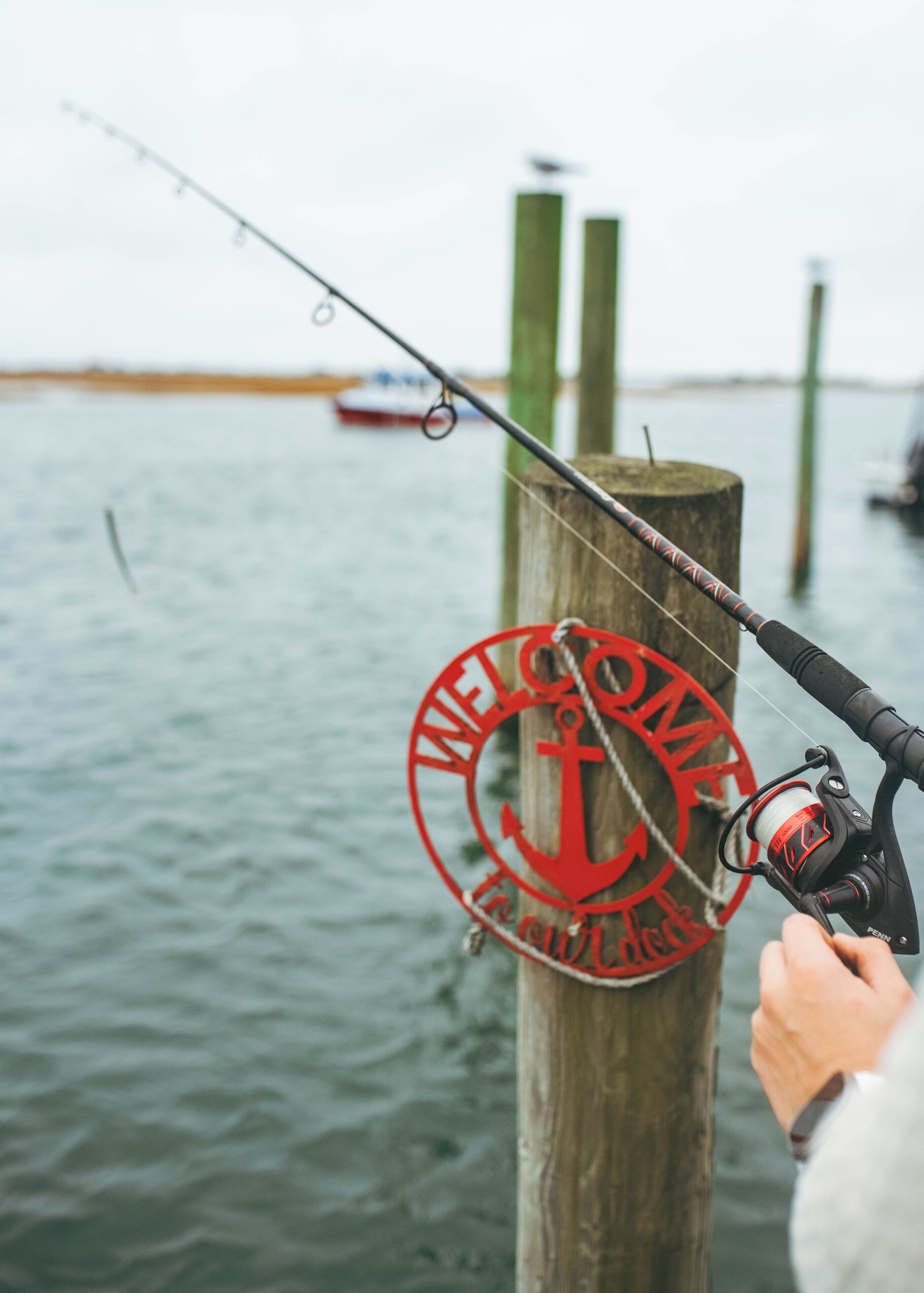 A fishing rod with a red "Welcome" sign attached to a wooden post by a body of water.