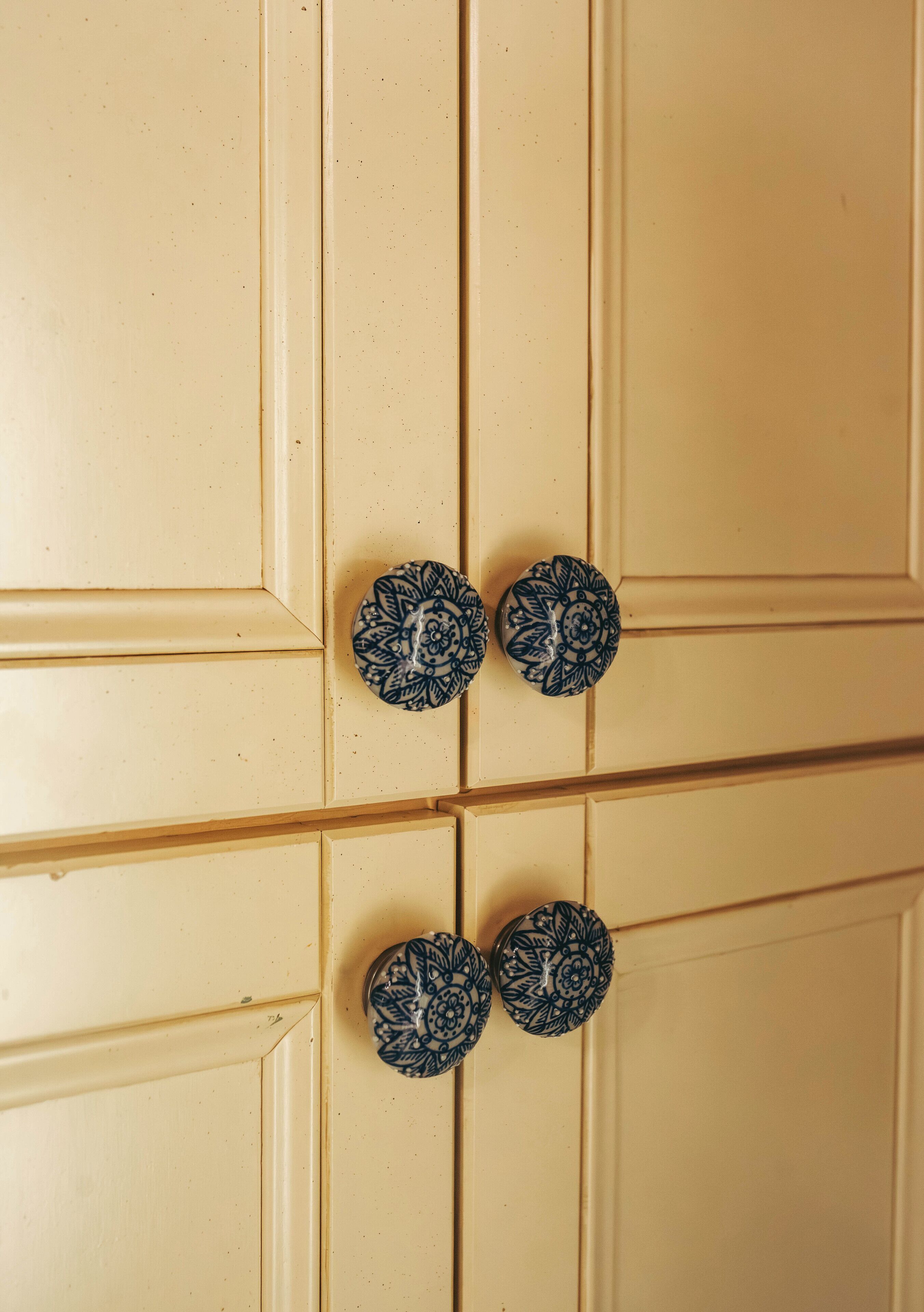 A beige wardrobe with four doors, each featuring a round, blue and white patterned knob.