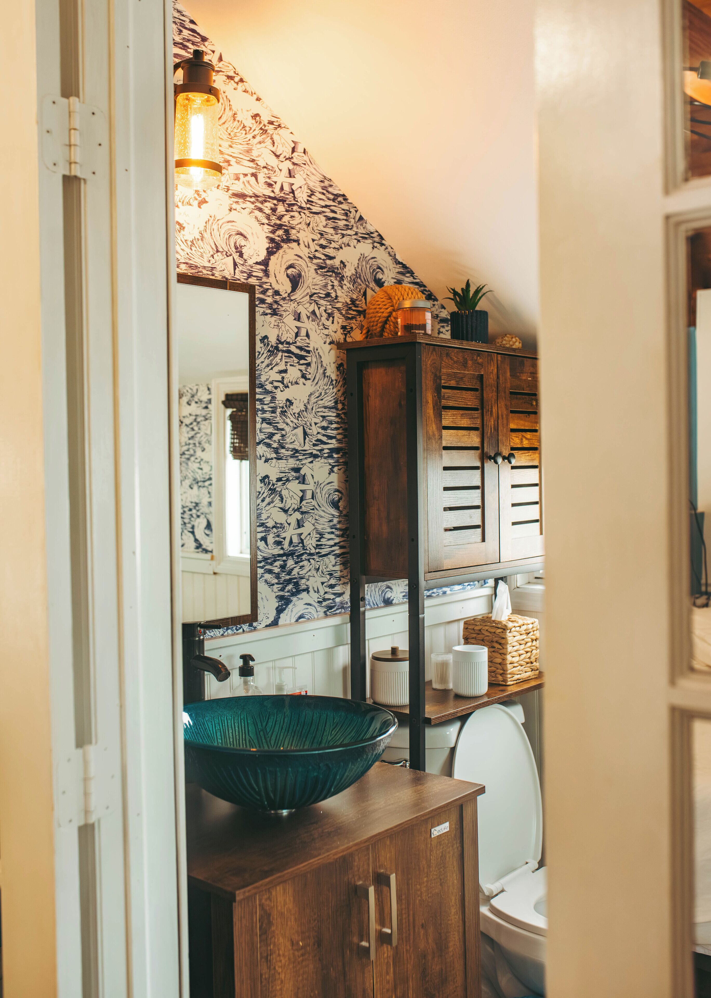 A bathroom with a wooden cabinet, a green bowl sink, a toilet, and a patterned wall.