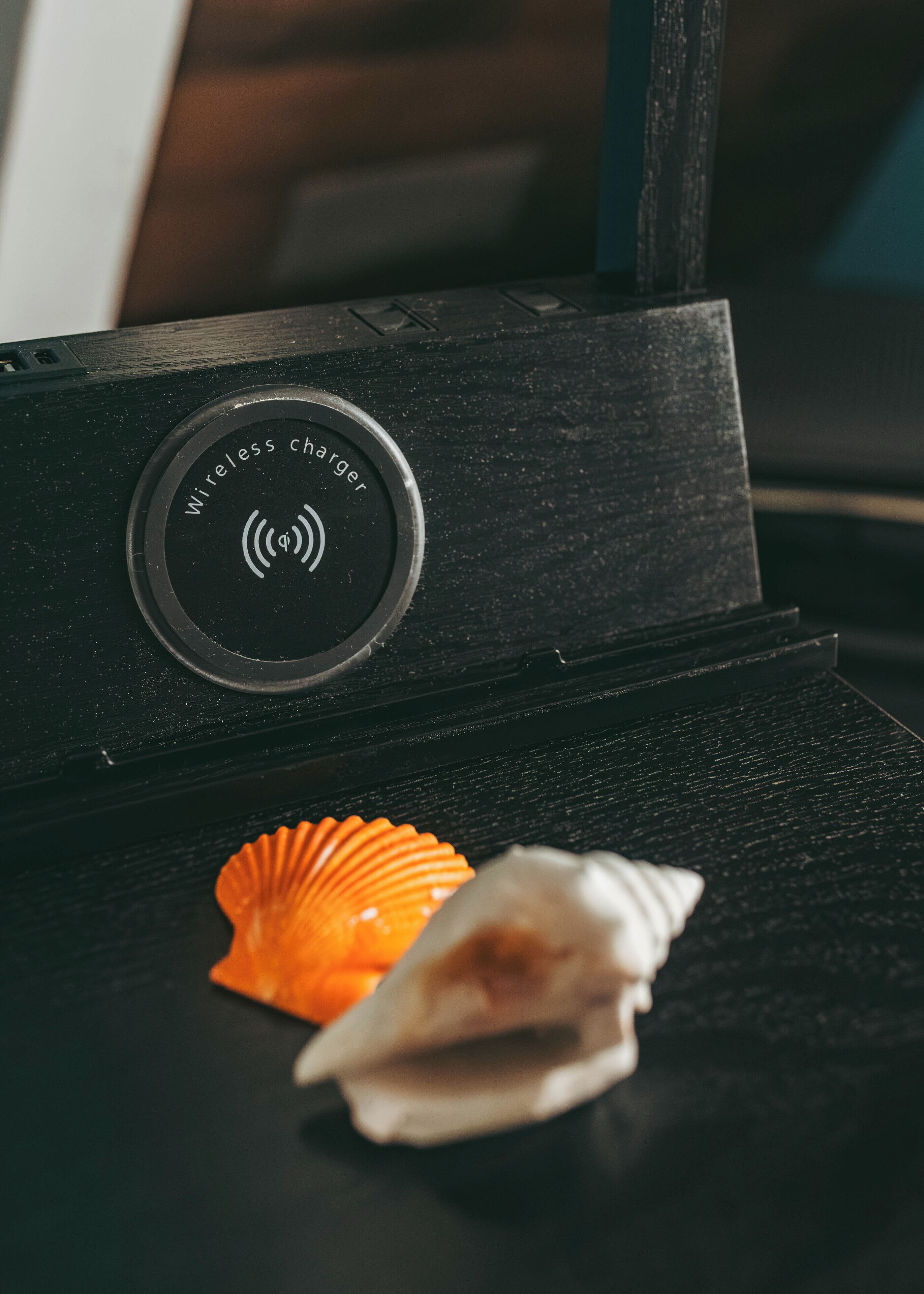 Un altoparlante nero con base di ricarica wireless e due conchiglie su un piano di legno.