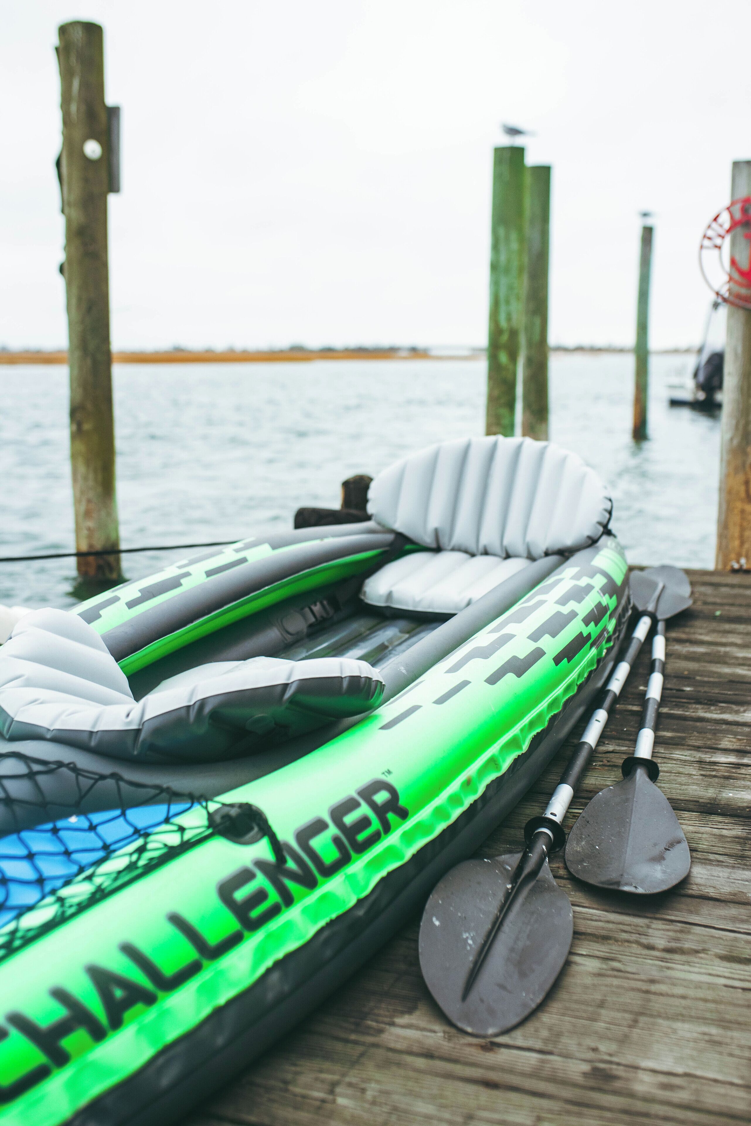 An inflatable raft with paddles and a net on a wooden dock by water.
