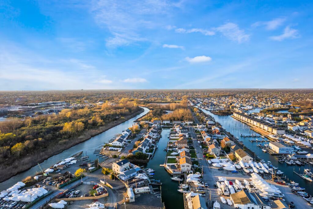 A marina with numerous boats docked along a river, surrounded by residential buildings and greenery.