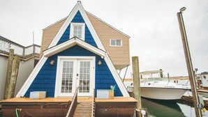 A boat house with a blue and beige exterior, a white door, and a wooden dock leading to it.