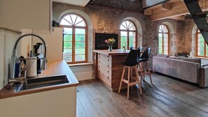 Una cocina con encimera de madera, un lavamanos y una zona de bar con taburetes. Hay ventanas de arco y una pared de piedra.
