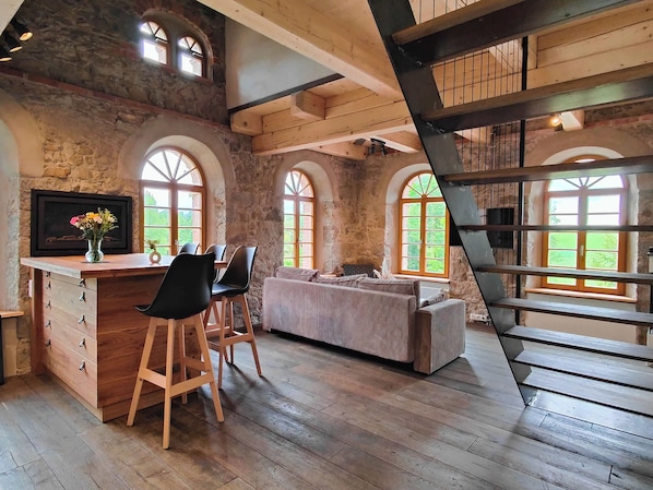 Ein rustikales Interieur mit Holzbalken, einer Sitzecke und großen Fenstern.