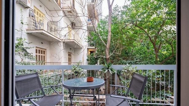 A balcony with two chairs and a table, overlooking a building with balconies and trees.