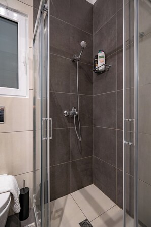 Une salle de bain moderne avec une douche à parois de verre, des murs recouverts de carreaux foncés, des toilettes blanches et un porte-serviettes.