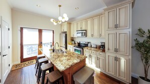 A spacious kitchen with granite countertops, a central island with stools, a large refrigerator, and a microwave. - Central house location! Private yard w/ Firepit, BBQ, 3 Kings, 75" TV, Parking (Columbus)
