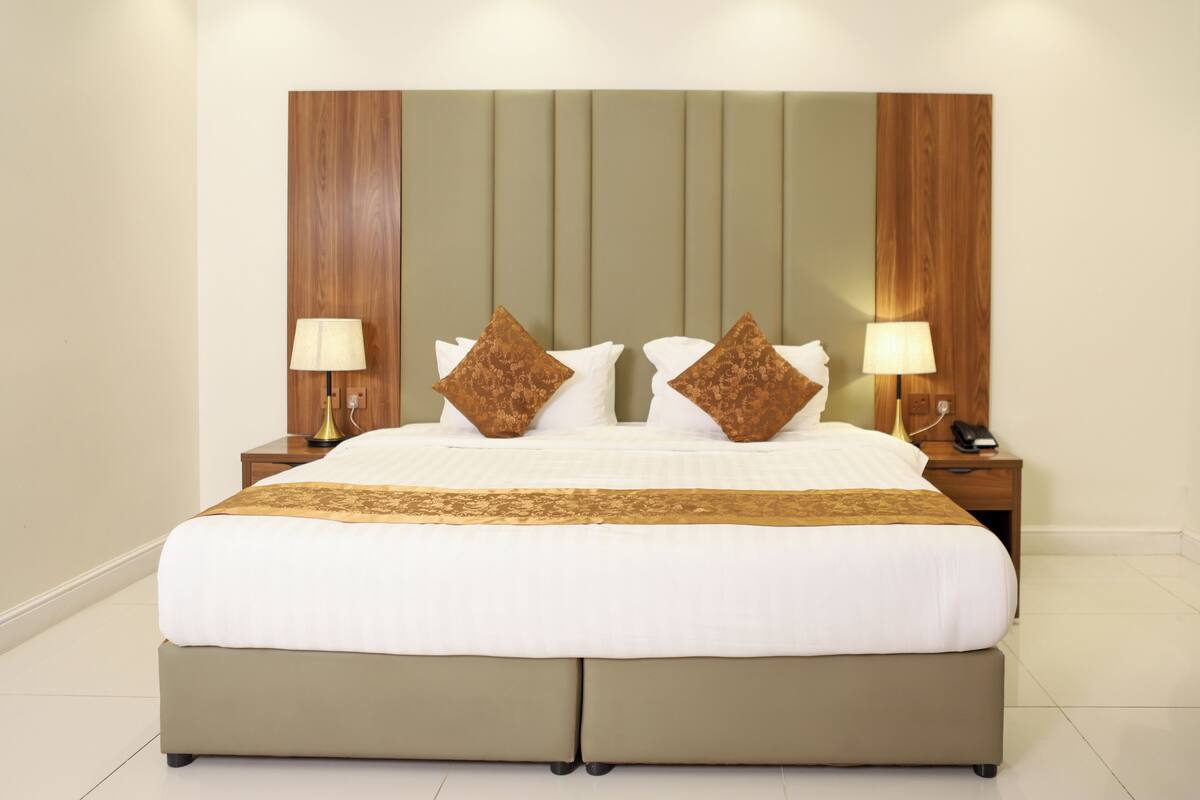 A large bed with a wooden headboard, two bedside tables with lamps, and a decorative pillow.