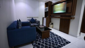 Un salon moderne avec un canapé bleu, une table basse et un téléviseur à écran plat fixé à un mur en bois.