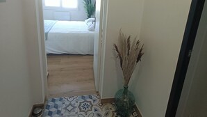 A hallway with patterned floor tiles, a bed in the background, a wall-mounted 'smile' sign, and a vase with dried plants. - Apartment 50m from the beach (Saint-Jean-de-Monts)