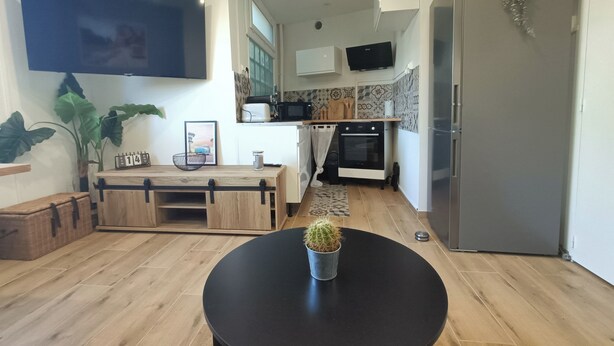 A modern kitchen with a wooden table, a black round table with a cactus, a refrigerator, and a microwave. - Apartment 50m from the beach (Saint-Jean-de-Monts)