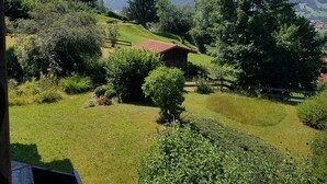 Ländliche Landschaft mit einem kleinen Haus, umgeben von Grünflächen, mit Bergen im Hintergrund.