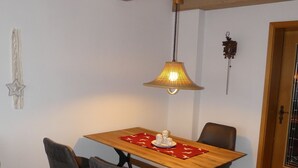 Ein Essbereich mit einem Holztisch, vier Stühlen, einer Hängelampe und einer Wanduhr.