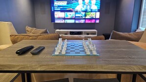 A living room with a chessboard, a TV displaying a sports channel, and a sofa. - Roswell Mini Mansion with Man Cave (Roswell)
