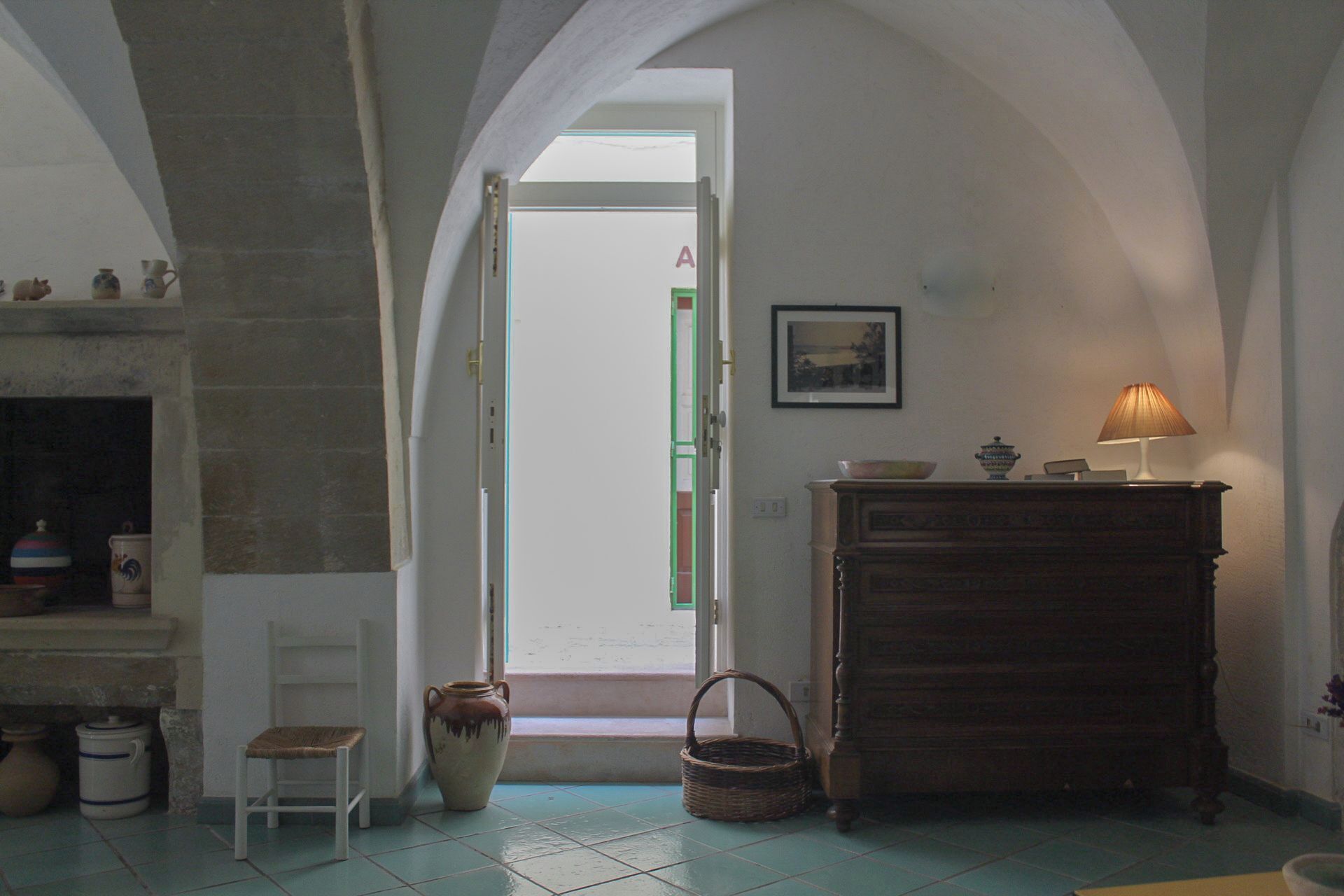 A room with a fireplace, a door leading to another room, a lamp, and a wooden cabinet.