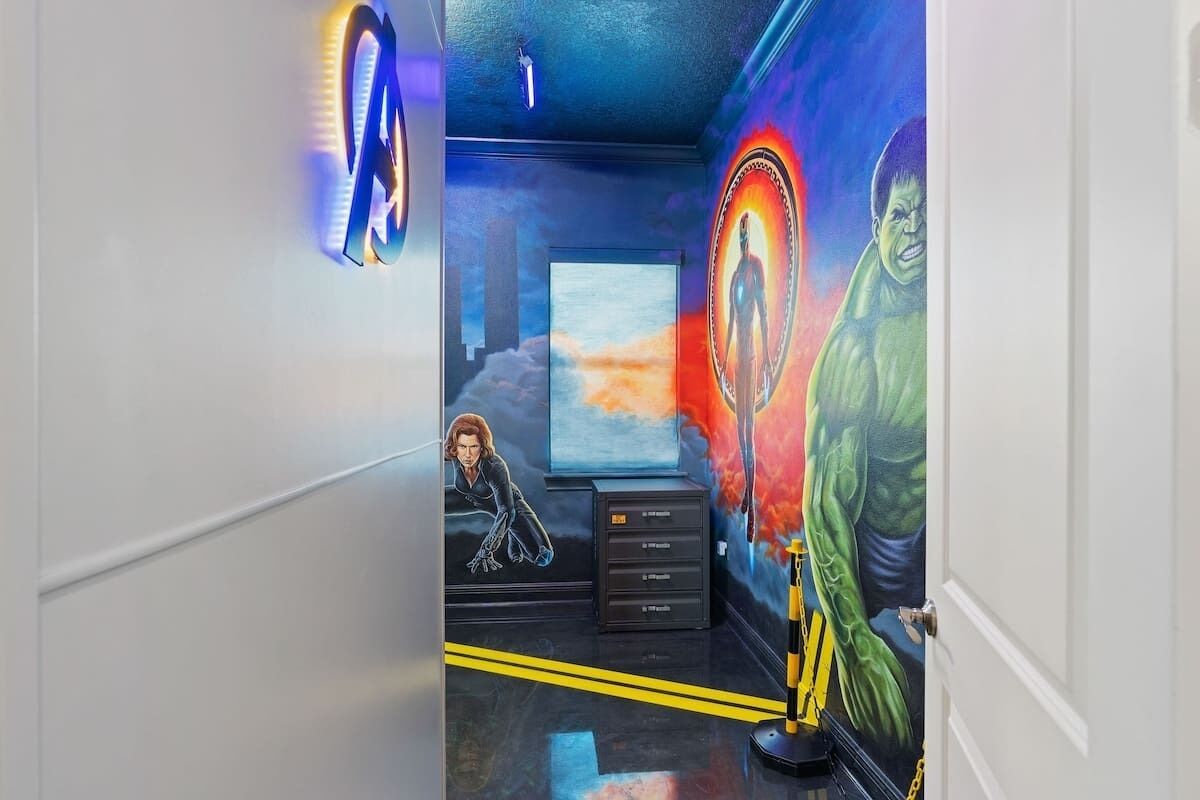 A room with a large mural of a green character, a TV screen, and a black cabinet with drawers.