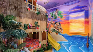 A room with a thatched-roof hut, a slide, and a mural of a tropical scene.