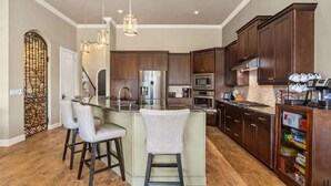 A modern kitchen with a central island, bar stools, stainless steel appliances, and dark wooden cabinets.