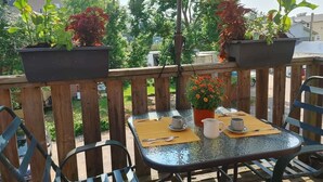 A wooden deck with a glass table and chairs, surrounded by potted plants and a large umbrella. - Pethick's Lookout Suite: Family-Friendly Apartment (Charlottetown)