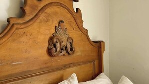 A bed with a wooden headboard featuring a carved crest, white linens, and a plain wall. - Pethick's Lookout Suite: Family-Friendly Apartment (Charlottetown)