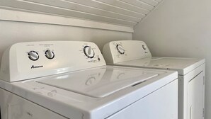 A white Amana front-loading washer and dryer set in a laundry room with a slanted ceiling. - Pethick's Lookout Suite: Family-Friendly Apartment (Charlottetown)