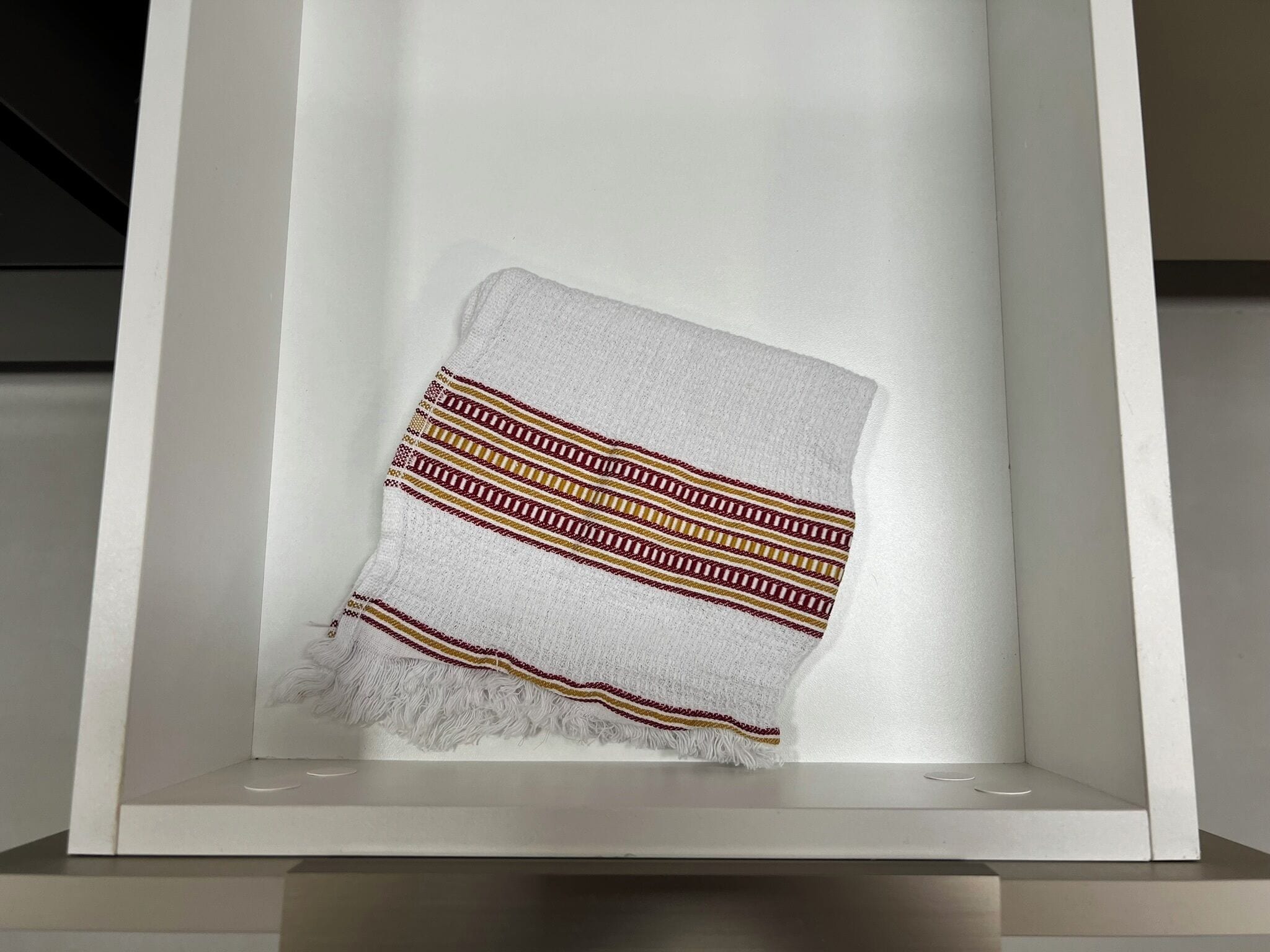 A framed textile with a geometric pattern, displayed in a white, minimalist setting.