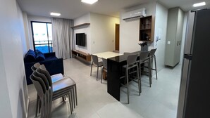 Ein modernes Wohnzimmer mit einer Couch, einem Esstisch mit Stühlen, einem an der Wand montierten Fernseher und einer Klimaanlage.