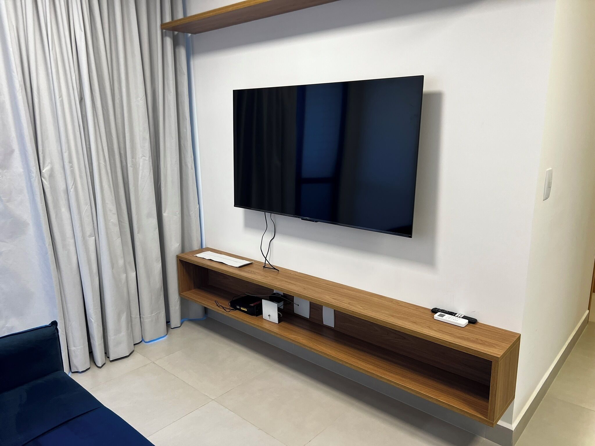 A modern living room with a mounted flat-screen TV, wooden TV stand, and a curtain.
