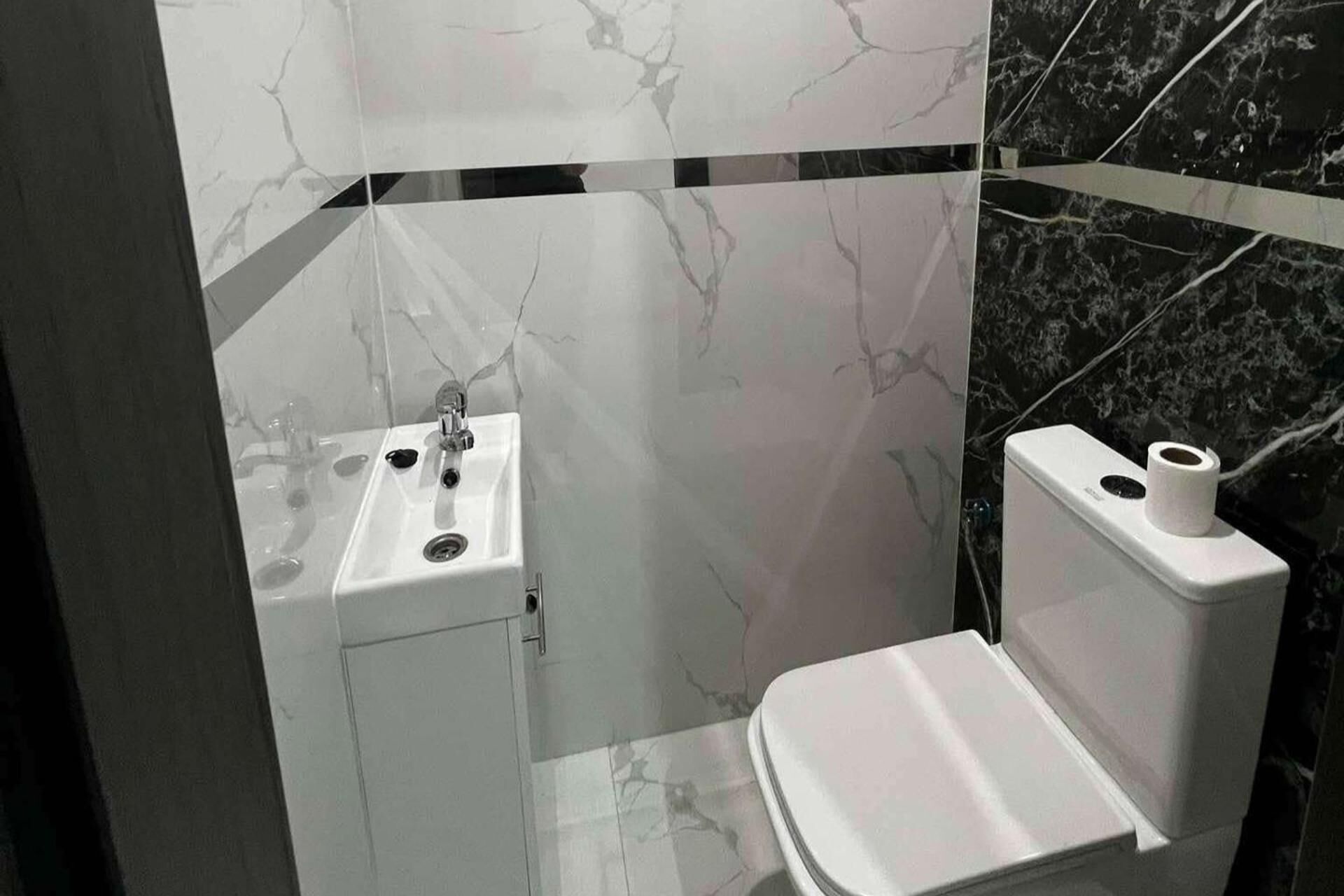 A modern bathroom with a white sink, toilet, and marble walls.