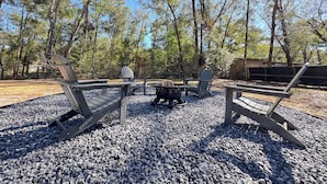 A campsite with Adirondack chairs, a fire pit, and a wooden table. - Charming Lake Town Home with WiFi (Inverness)