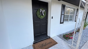 A house with a black front door, a welcome mat, a wreath, and a window with shutters. - Charming Lake Town Home with WiFi (Inverness)