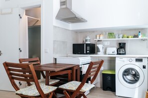 Una cucina compatta con tavolo e sedie, lavatrice, forno a microonde e macchina del caffè.