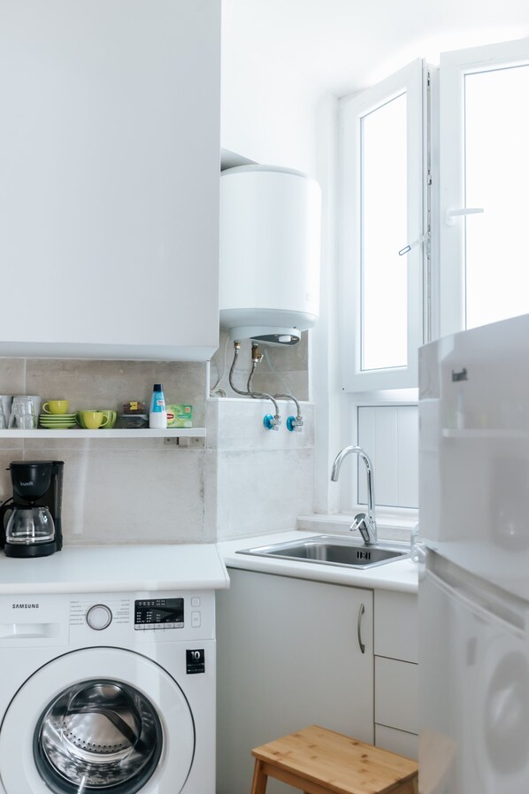 A compact kitchen with a washing machine, a coffee maker, a sink, and a window.