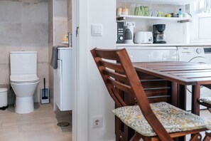 Una cucina compatta con lavandino, fornello e microonde. C'è un tavolo da pranzo con sedie e una finestra che lascia entrare luce naturale.