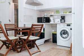 Una cucina compatta con un tavolo e sedie, un forno a microonde, una macchina per il caffè e una lavatrice.