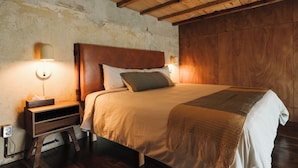 Een slaapkamer met een houten hoofdbord, een nachtkastje met een lamp, en een bed met een deken.