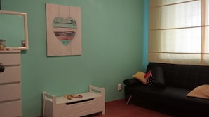 Una habitación con paredes verde mar, un aparador blanco, una cama pequeña para niño en blanco, un sofá negro y una ventana con cortinas.