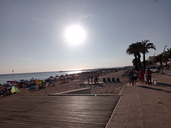 A wooden boardwalk leading to a beach with umbrellas and people.