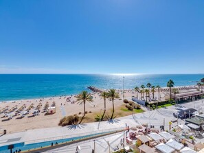 A beach resort with a pool, sun loungers, and palm trees.