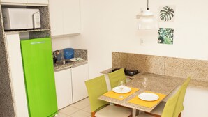A compact kitchen with a green refrigerator, granite countertops, and a dining area with four chairs and a table set for two. - Marupiara Flat, equipped, free Wi-Fi and parking, best part of the beach (N. São do Ó)