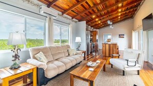 A cozy living room with a wooden ceiling, a sofa, a coffee table, and a dining area. - Loggerhead - 2BR House at Secret Beach (San Pedro)
