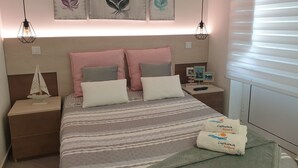 A neatly arranged bedroom with a bed, two nightstands, and a headboard. There are decorative feather paintings on the wall, a small sailboat model on one nightstand, and a remote control on the other. - Light Wave Nazare Center 50m Beach (Nazaré)