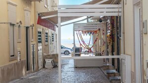 A narrow street with a covered outdoor seating area, a car parked on the side, and a view of the beach. - Light Wave Nazare Center 50m Beach (Nazaré)