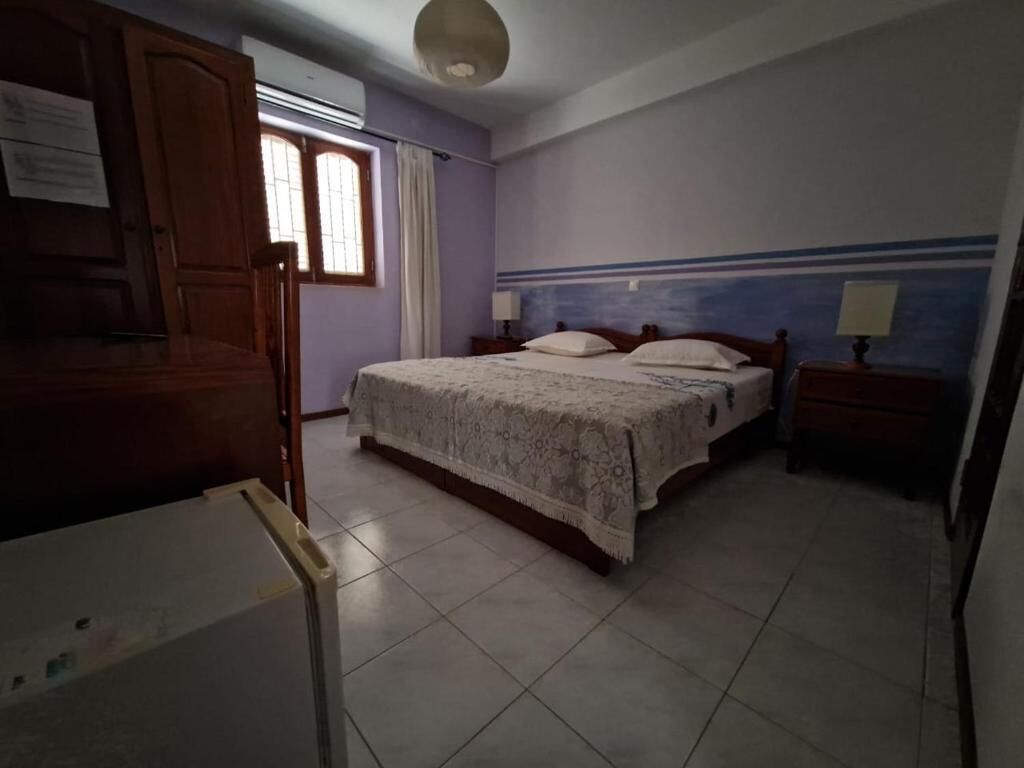 Une chambre à coucher comprenant un lit, une table de chevet, une armoire et une fenêtre avec des rideaux.