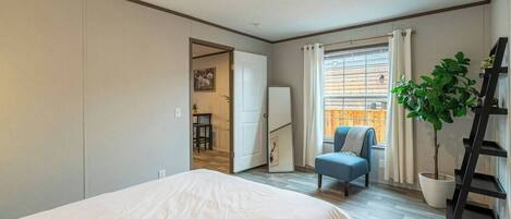 A bedroom with a bed, a chair, a potted plant, a ladder, and a view of an outdoor balcony.